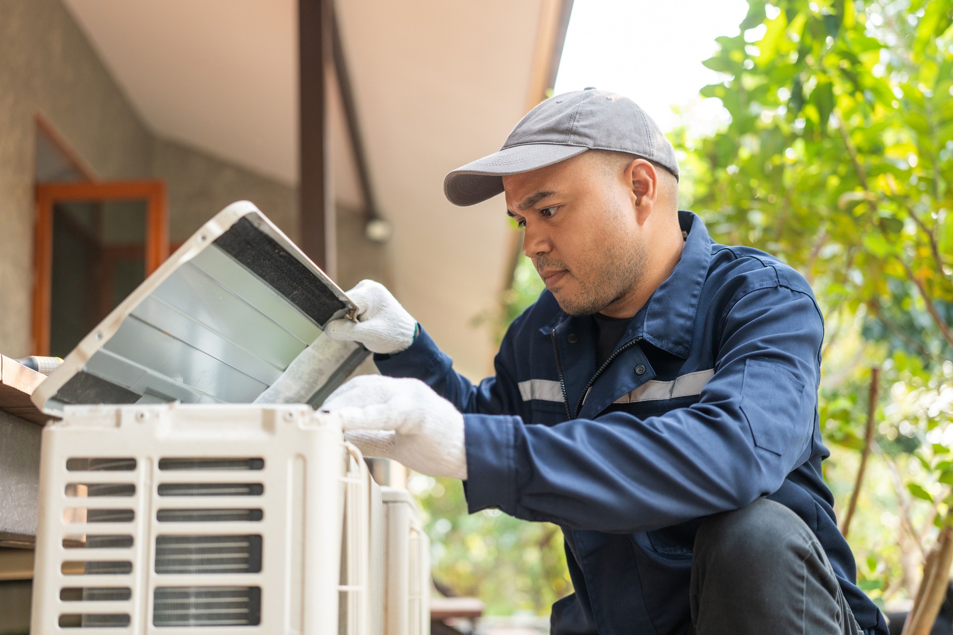 Air conditioner service outdoor checking fix repair. Air conditioner cleaning technician He opened the front cover and took out the filters and washed it. He in uniform wearing rubber